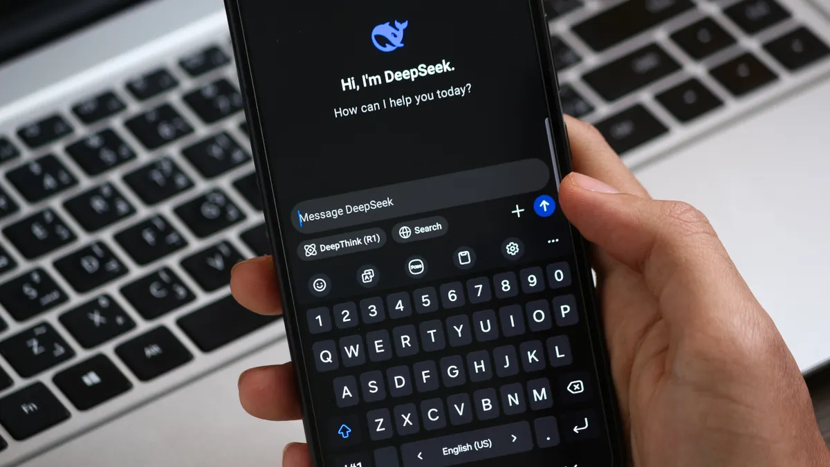 Hand holding phone with AI chat app over laptop