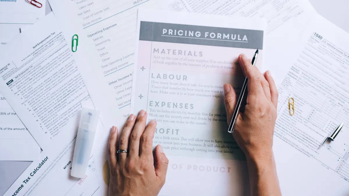 hands filling out a pricing formula sheet on a desk