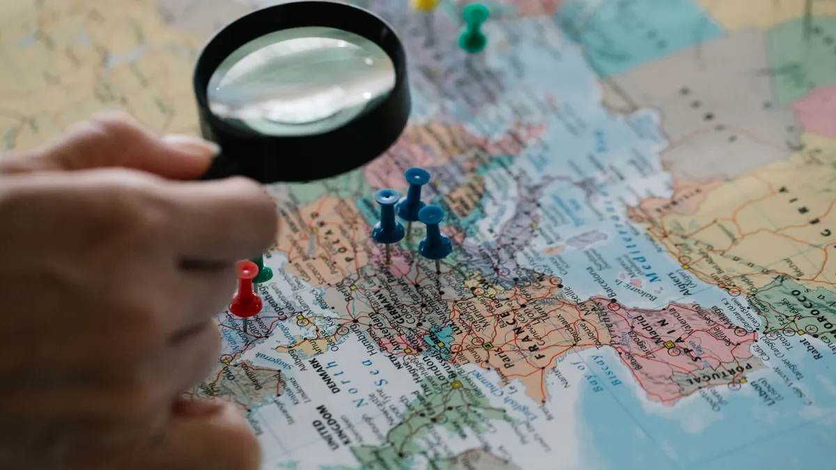 hand holding magnifying glass over a map with push pins