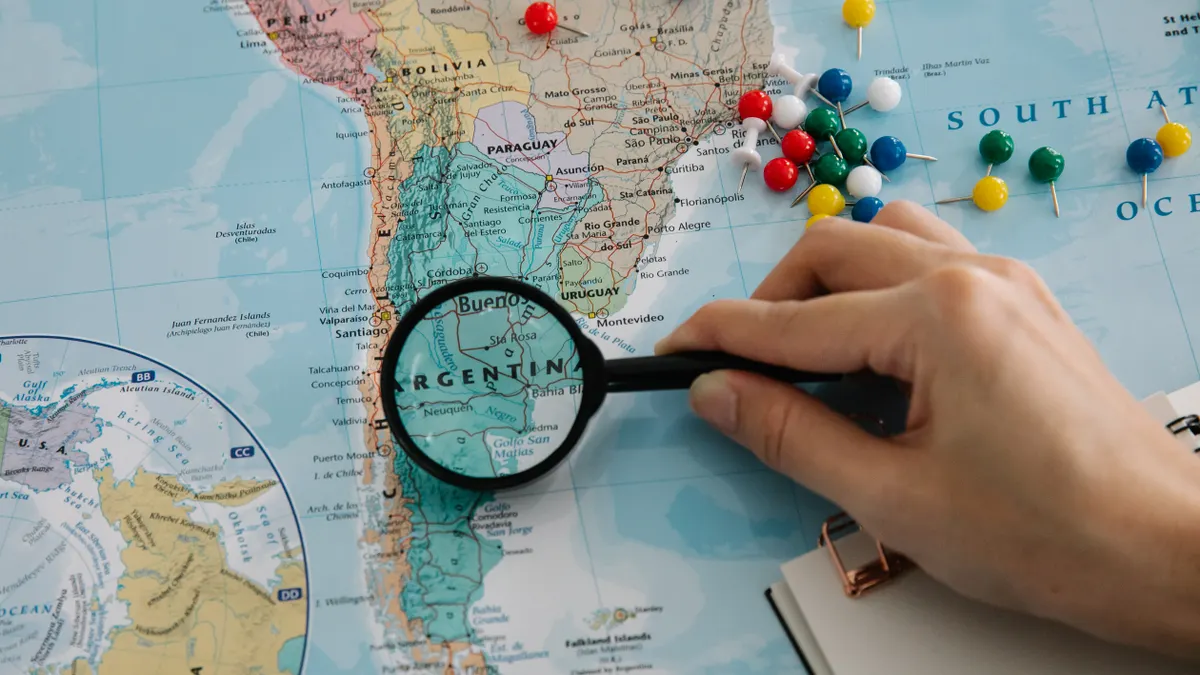 hand using magnifying glass on a map with many push pins